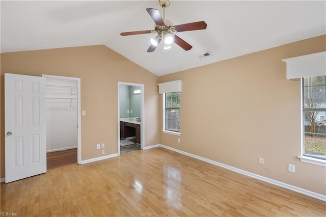 unfurnished bedroom with ensuite bath, light hardwood / wood-style flooring, a spacious closet, vaulted ceiling, and a closet