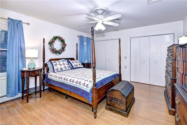 bedroom with ceiling fan, light hardwood / wood-style flooring, a baseboard radiator, and multiple closets