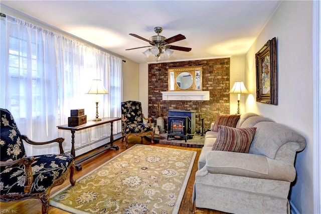 sitting room featuring wood-type flooring, a wood stove, ceiling fan, and baseboard heating