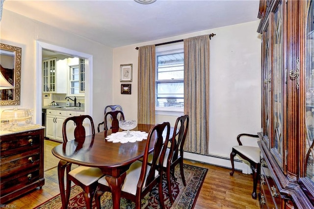 dining space with sink, light wood-type flooring, and baseboard heating