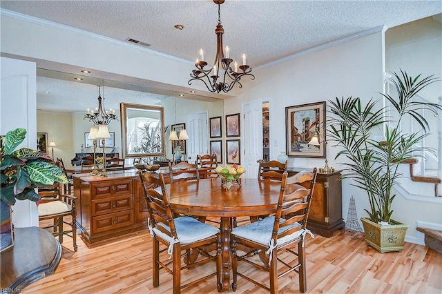 dining space featuring ornamental molding, light wood-type flooring, a textured ceiling, and a notable chandelier