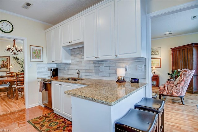 kitchen with sink, white cabinetry, light stone counters, stainless steel dishwasher, and ornamental molding