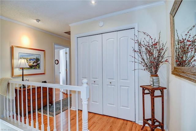 corridor with ornamental molding, a textured ceiling, and light wood-type flooring