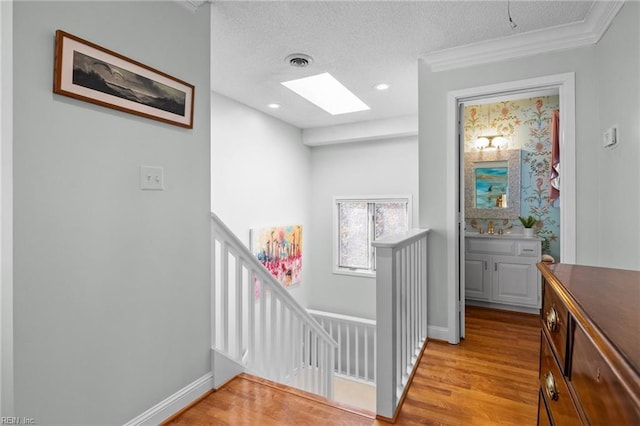 hall featuring crown molding, a skylight, a textured ceiling, and light wood-type flooring