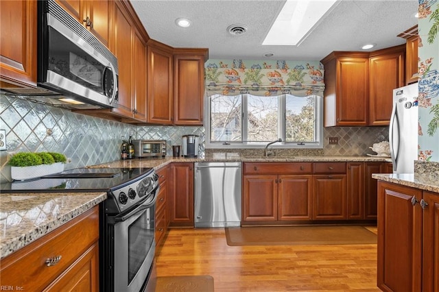 kitchen with light stone countertops, a skylight, stainless steel appliances, and light hardwood / wood-style floors