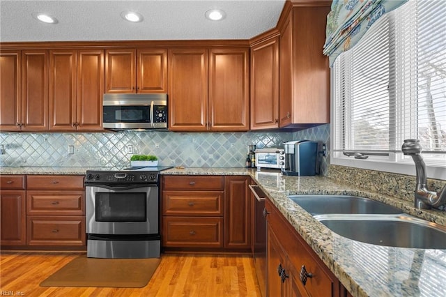 kitchen with appliances with stainless steel finishes, sink, backsplash, light stone counters, and light hardwood / wood-style floors