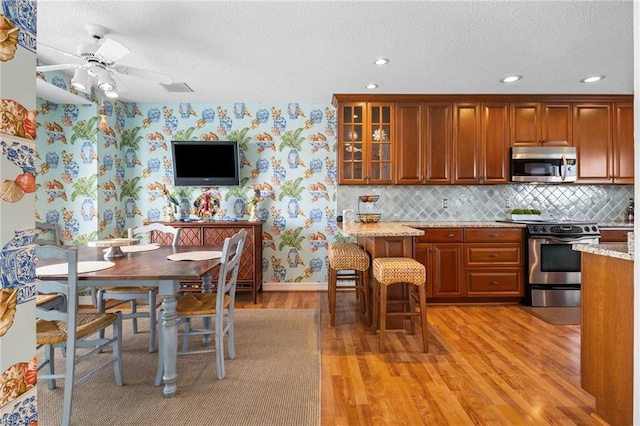 kitchen with light hardwood / wood-style flooring, a breakfast bar area, ceiling fan, stainless steel appliances, and light stone counters