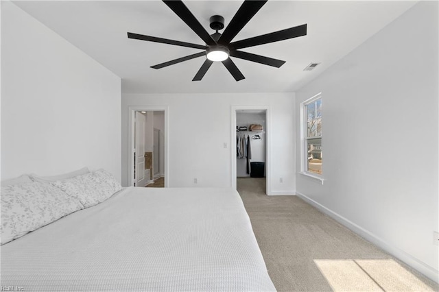 unfurnished bedroom featuring ceiling fan, ensuite bathroom, a spacious closet, light colored carpet, and a closet