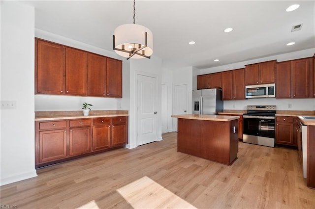 kitchen with pendant lighting, a kitchen island, light hardwood / wood-style flooring, and appliances with stainless steel finishes