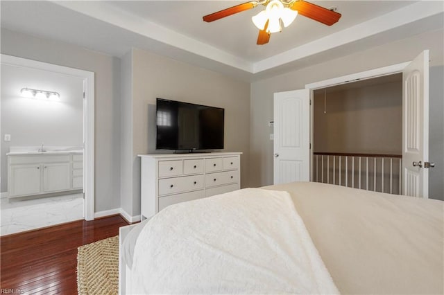 bedroom featuring ensuite bathroom, sink, dark hardwood / wood-style flooring, a raised ceiling, and ceiling fan