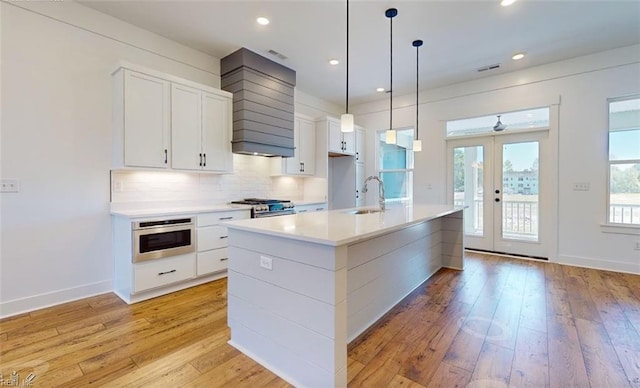 kitchen featuring french doors, appliances with stainless steel finishes, white cabinets, and a center island with sink