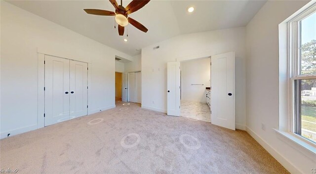 unfurnished bedroom with connected bathroom, vaulted ceiling, light colored carpet, and multiple closets