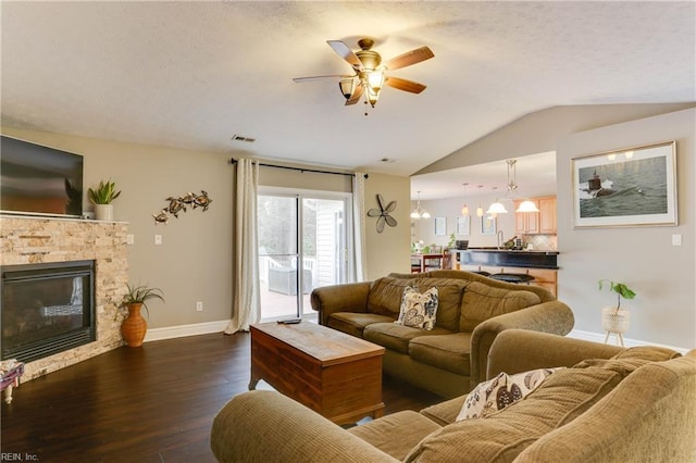 living room featuring a stone fireplace, dark wood-type flooring, ceiling fan with notable chandelier, and vaulted ceiling