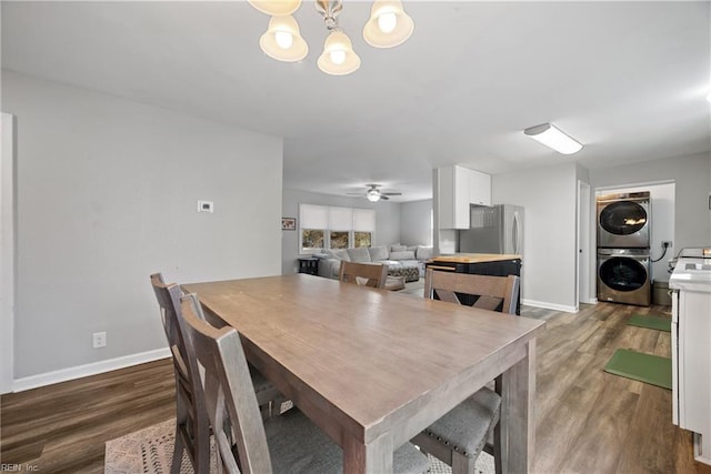 dining space with stacked washer / drying machine, ceiling fan with notable chandelier, and dark wood-type flooring