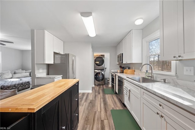 kitchen with appliances with stainless steel finishes, stacked washer / drying machine, sink, and white cabinets