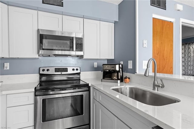 kitchen with white cabinetry, stainless steel appliances, light stone countertops, and sink