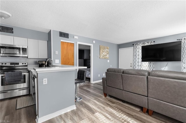 kitchen with a breakfast bar area, a kitchen island with sink, hardwood / wood-style floors, stainless steel appliances, and white cabinets