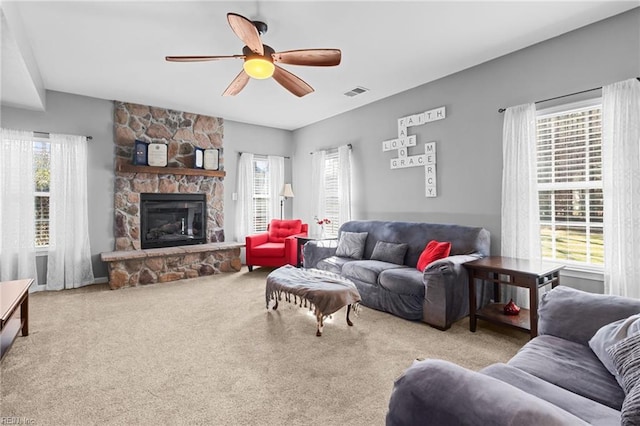 carpeted living room featuring ceiling fan, a healthy amount of sunlight, and a stone fireplace