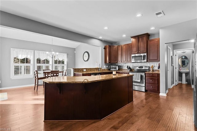 kitchen with a breakfast bar area, hanging light fixtures, appliances with stainless steel finishes, kitchen peninsula, and decorative backsplash