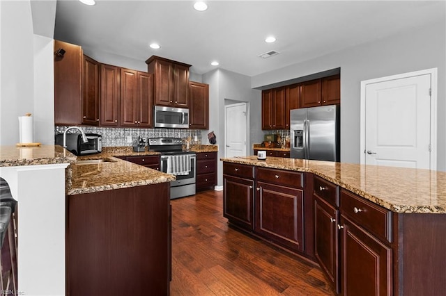 kitchen with appliances with stainless steel finishes, sink, dark hardwood / wood-style flooring, decorative backsplash, and kitchen peninsula