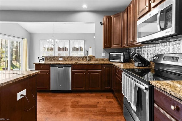 kitchen featuring stainless steel appliances, sink, pendant lighting, and stone counters