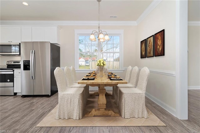 dining area with ornamental molding, an inviting chandelier, and light wood-type flooring