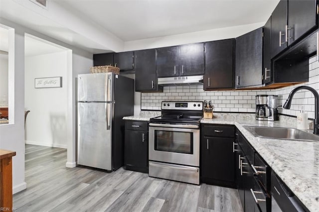 kitchen featuring sink, light stone counters, stainless steel appliances, light hardwood / wood-style floors, and backsplash