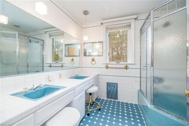 bathroom with tile walls, vanity, a wealth of natural light, and bath / shower combo with glass door