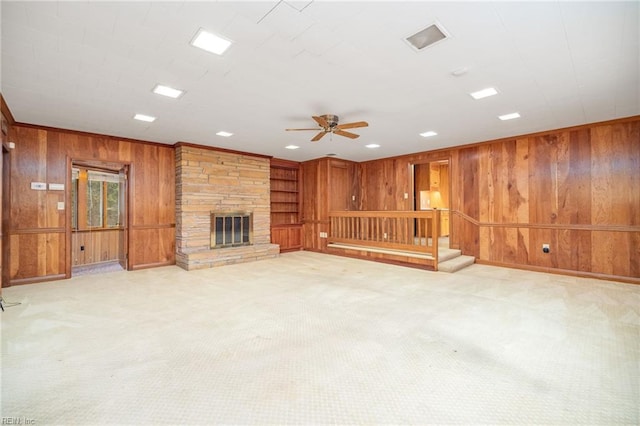 unfurnished living room featuring light colored carpet, a stone fireplace, and wood walls