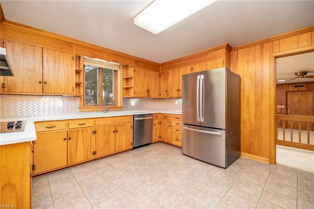 kitchen with sink, wood walls, ceiling fan, stainless steel appliances, and backsplash