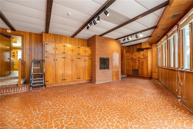 unfurnished living room with beamed ceiling, rail lighting, and wood walls