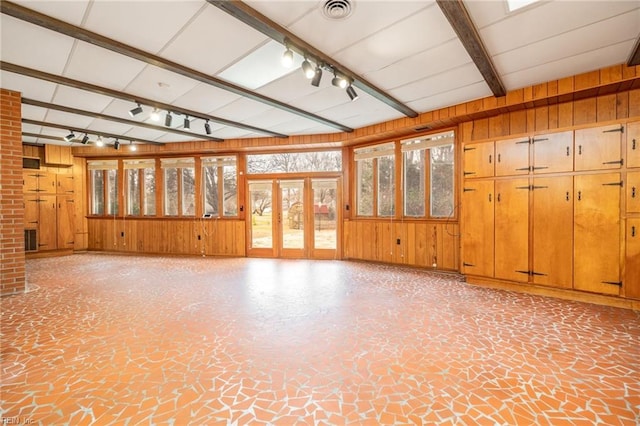 unfurnished living room with wooden walls, beamed ceiling, and track lighting