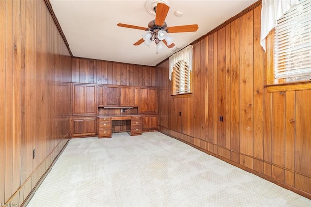 office area featuring ceiling fan, built in desk, light carpet, and wood walls