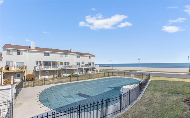 view of pool featuring a water view, a yard, a view of the beach, and a patio area