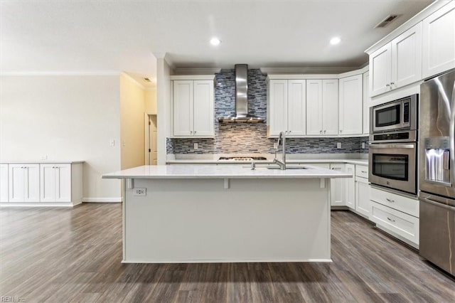 kitchen featuring sink, wall chimney range hood, an island with sink, stainless steel appliances, and white cabinets