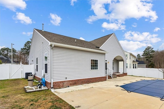 back of house featuring central AC unit, a patio area, a covered pool, and a lawn