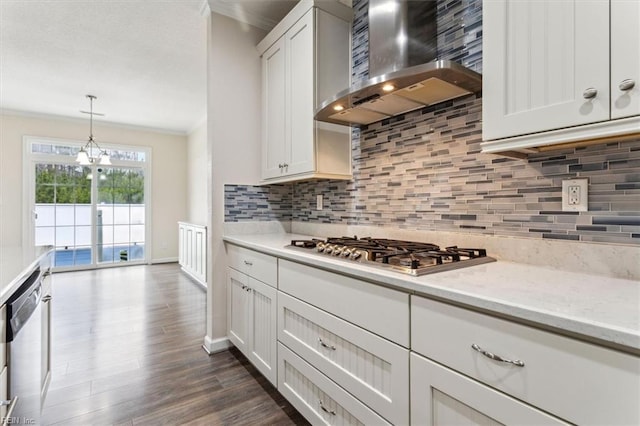 kitchen featuring wall chimney exhaust hood, white cabinetry, appliances with stainless steel finishes, pendant lighting, and light stone countertops