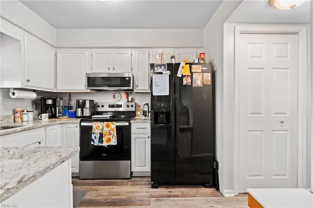 kitchen with stainless steel appliances, light stone counters, white cabinets, and light hardwood / wood-style floors