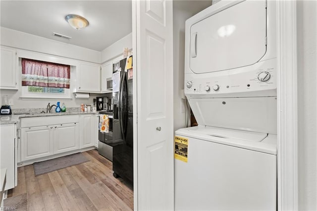 laundry area with stacked washer / drying machine, sink, and light hardwood / wood-style flooring