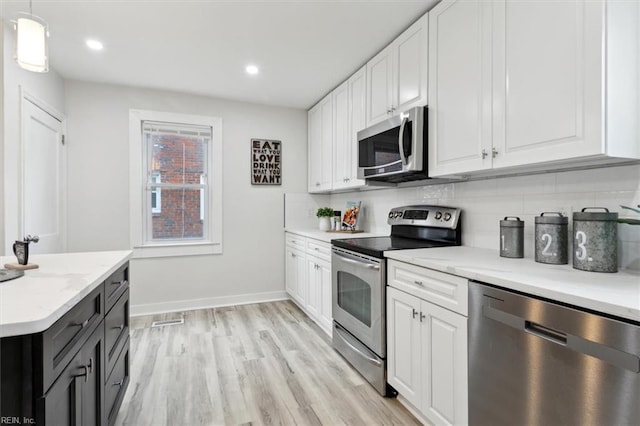 kitchen featuring hanging light fixtures, backsplash, white cabinets, and appliances with stainless steel finishes