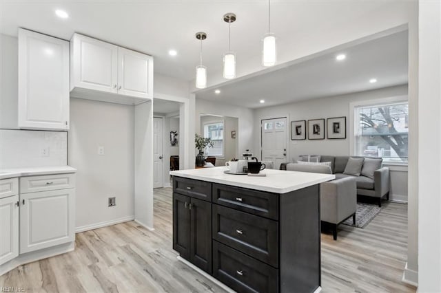 kitchen with a kitchen island, tasteful backsplash, white cabinetry, hanging light fixtures, and light hardwood / wood-style flooring