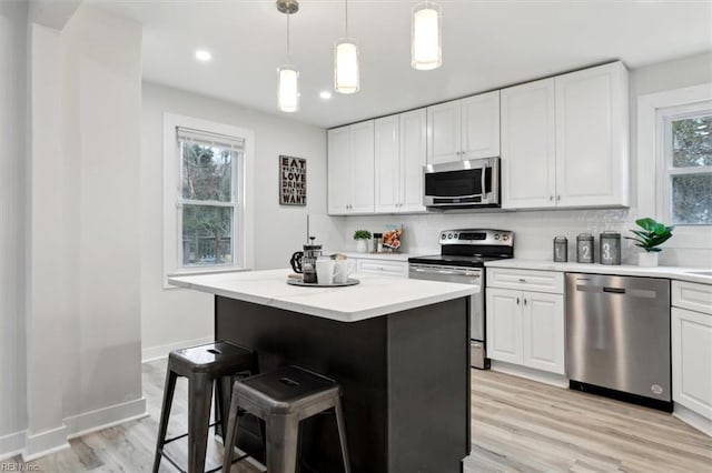 kitchen with decorative light fixtures, stainless steel appliances, white cabinets, and a kitchen island