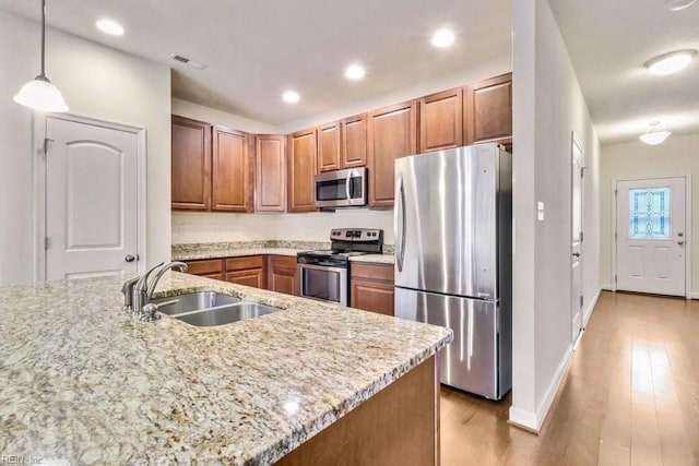 kitchen featuring sink, decorative light fixtures, light wood-type flooring, stainless steel appliances, and light stone countertops