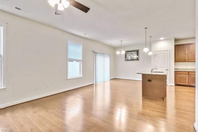 unfurnished living room featuring sink, ceiling fan with notable chandelier, and light wood-type flooring