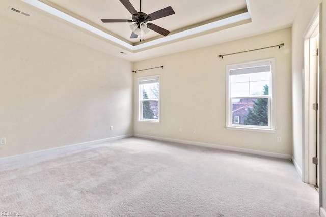 unfurnished room with ceiling fan, light colored carpet, and a tray ceiling