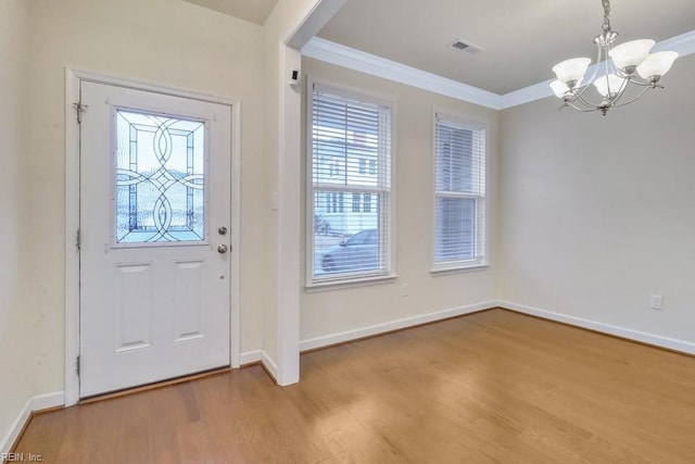 entrance foyer featuring hardwood / wood-style flooring, ornamental molding, plenty of natural light, and a chandelier