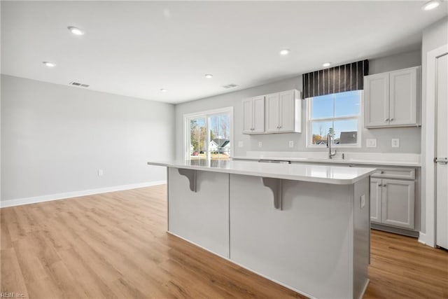 kitchen with sink, a breakfast bar, white cabinetry, a center island, and light hardwood / wood-style floors