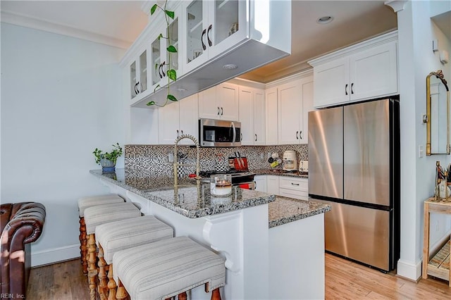 kitchen featuring stainless steel appliances, kitchen peninsula, dark stone counters, and white cabinets