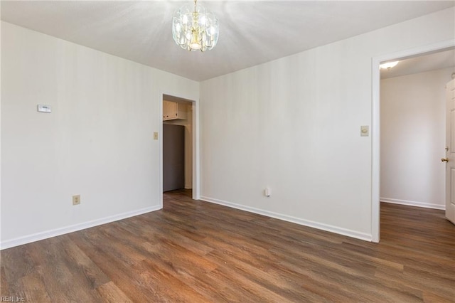 empty room with dark wood-type flooring and a chandelier