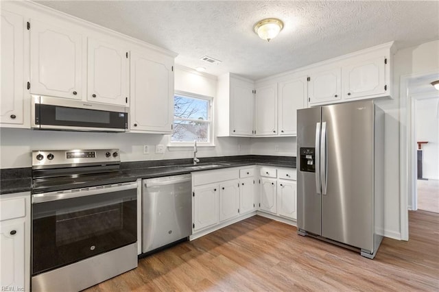 kitchen with sink, white cabinetry, a textured ceiling, light wood-type flooring, and stainless steel appliances